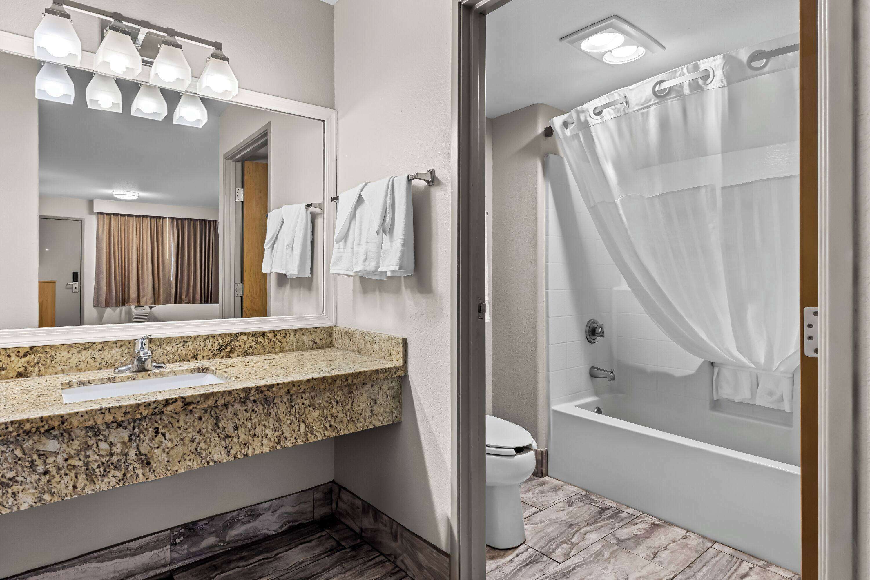 A modern bathroom with a granite countertop sink, a large mirror, and a glass-enclosed shower.