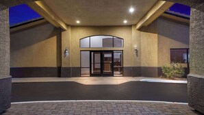 A hotel entrance with a brick-paved driveway, a glass door entrance, and a small landscaped area with a plant. - Days Inn by Wyndham Buckeye (Buckeye)