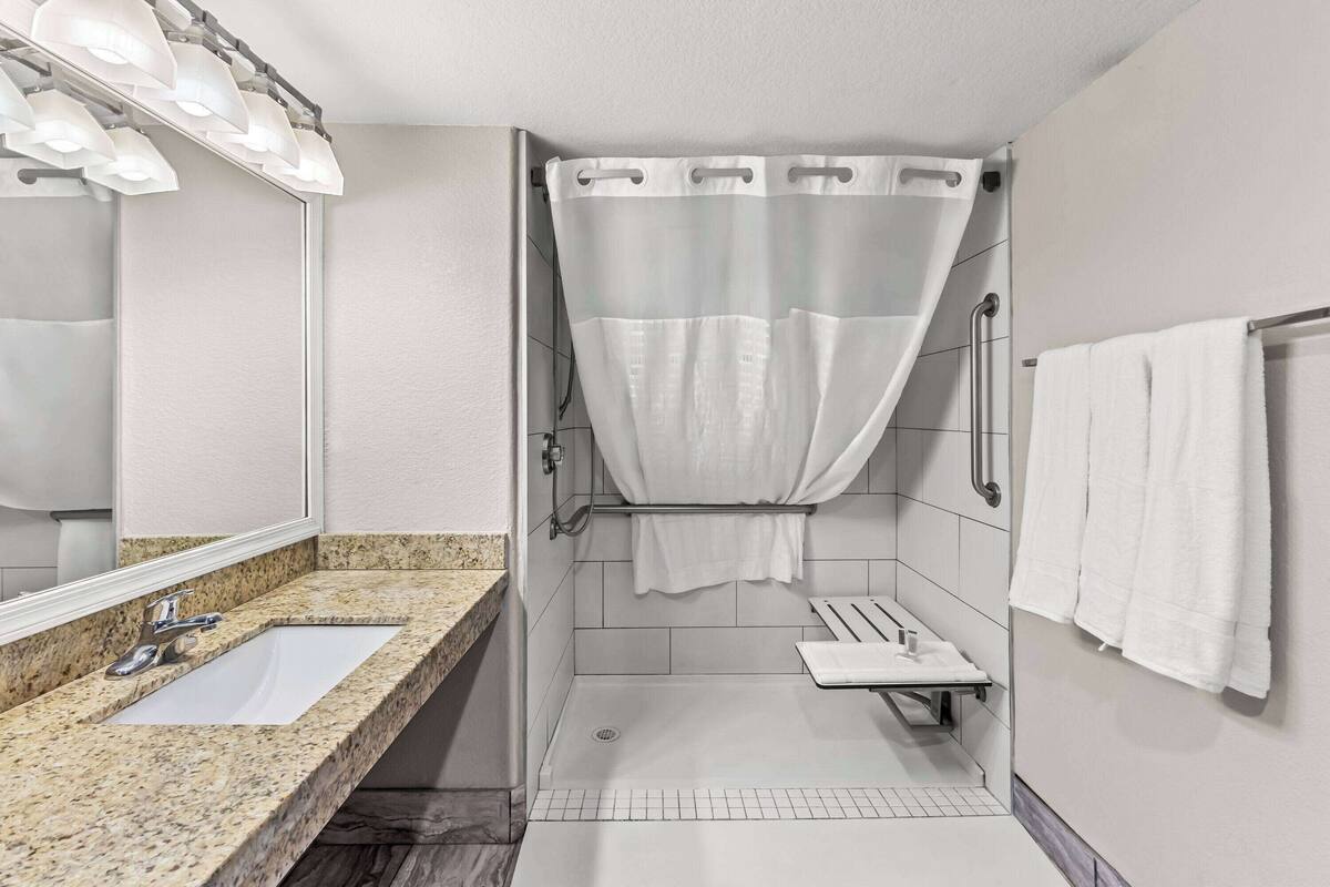 A modern bathroom with a granite countertop sink, a glass shower enclosure, and a towel rack.