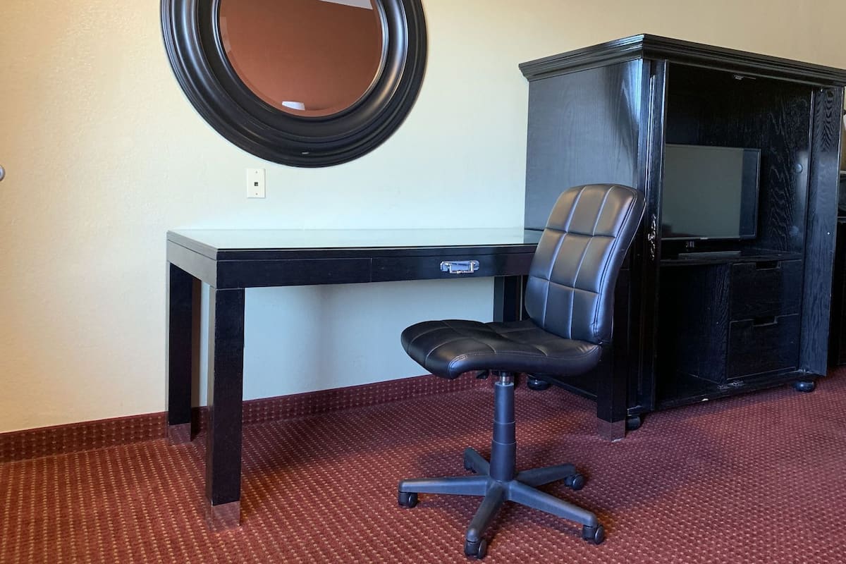 A hotel room with a desk, a chair, a television, and a mirror.