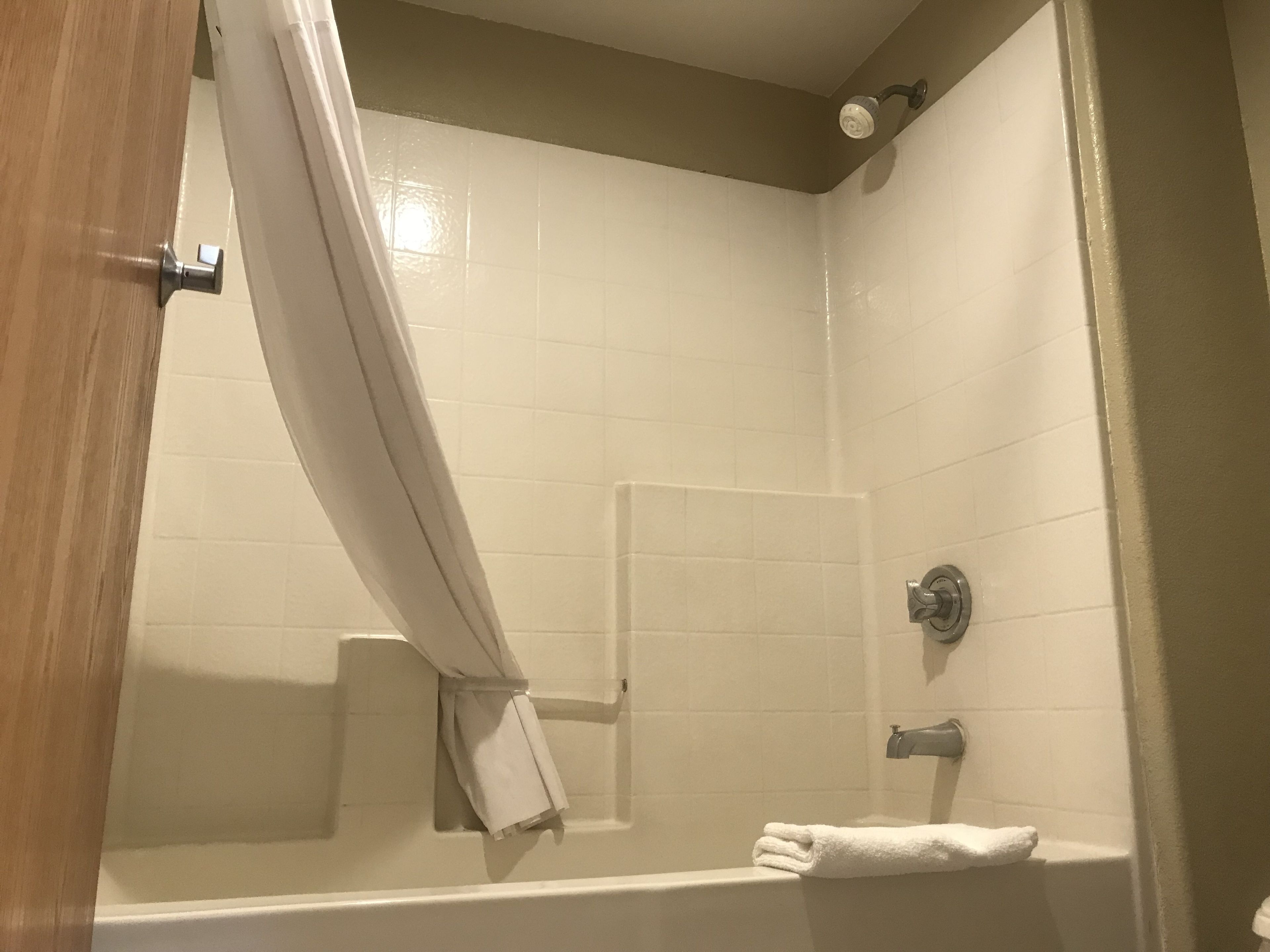 A bathroom with white tiled walls, a bathtub, a shower curtain, and a towel rack.
