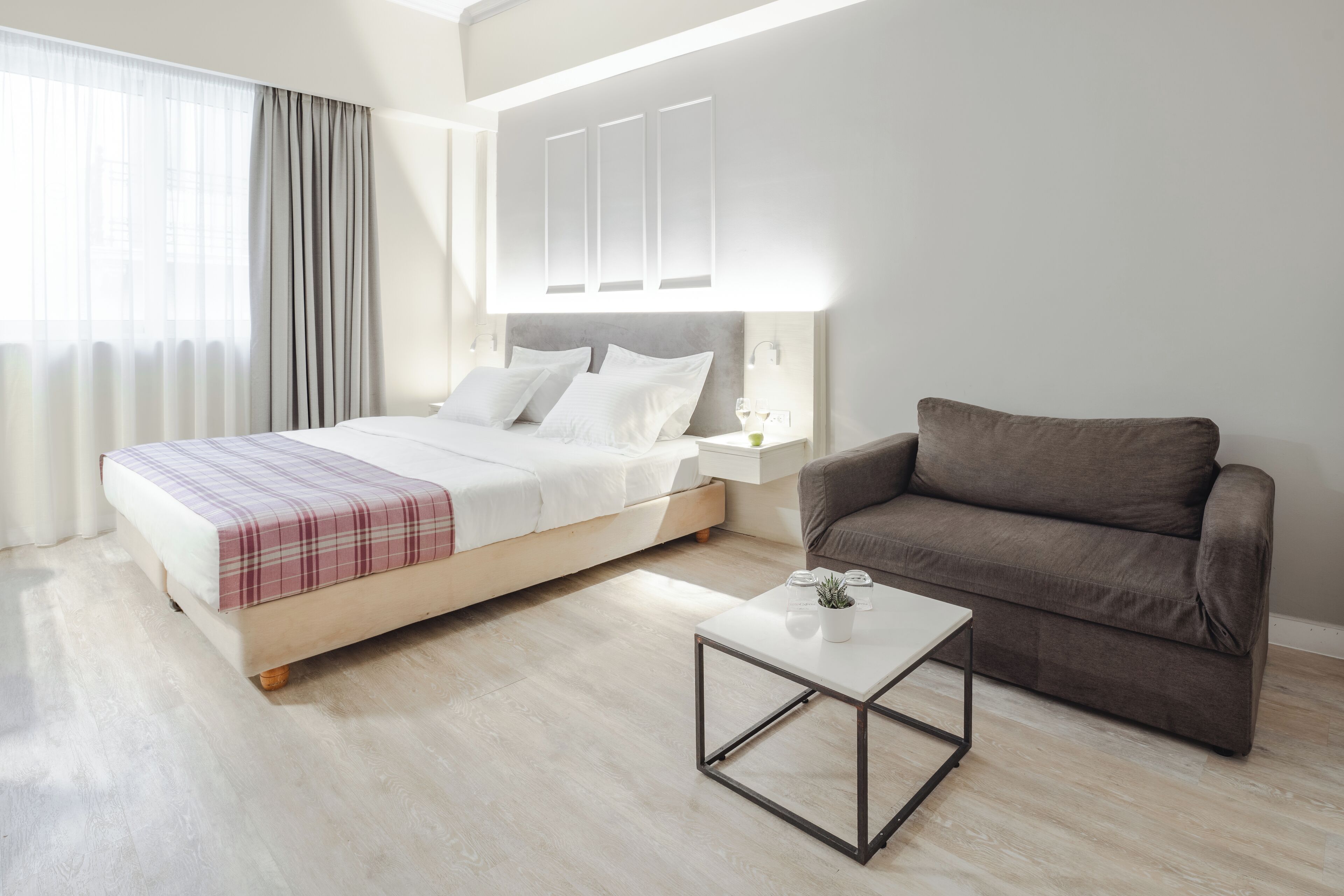 A modern hotel room with a bed, a sofa, a coffee table, and a nightstand.