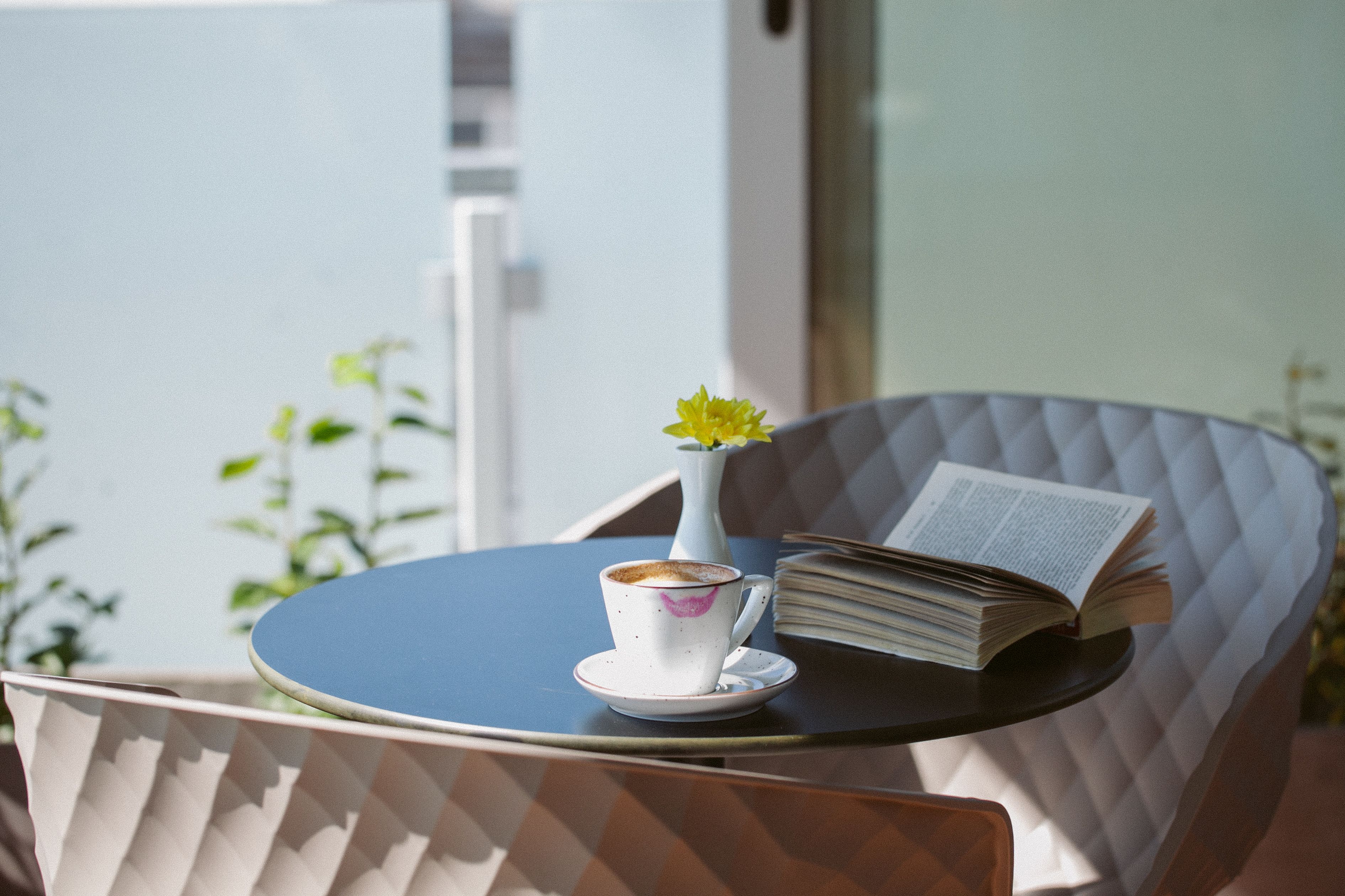 A table with a cup of coffee, a book, and a vase with a flower.