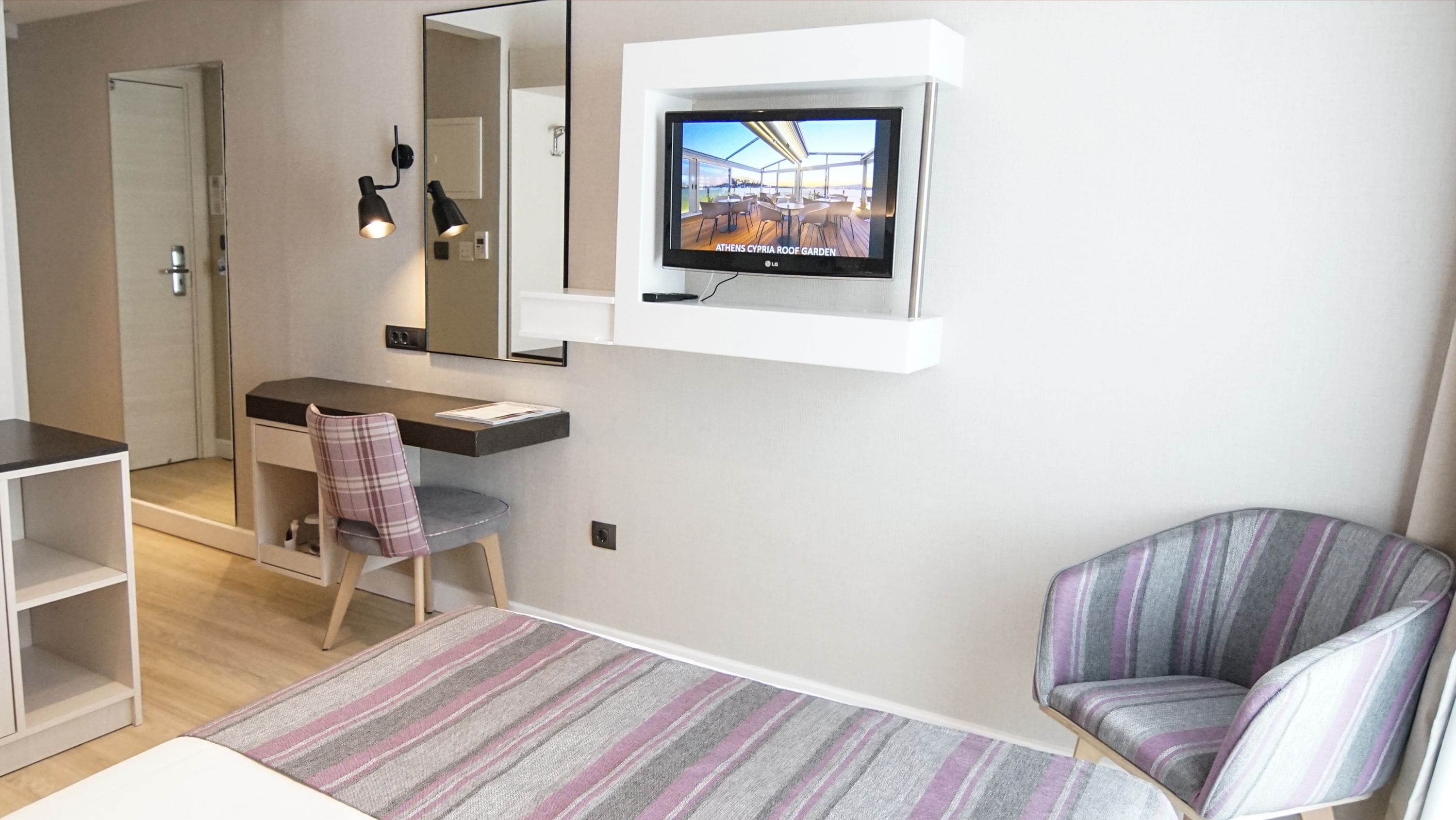 Una habitación de hotel moderna con una televisión de pantalla plana montada en la pared, un escritorio con una silla, un tapete a rayas y un sillón a rayas.