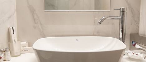 A bathroom with a large oval sink, a mirror above it, and toiletries on the counter.
