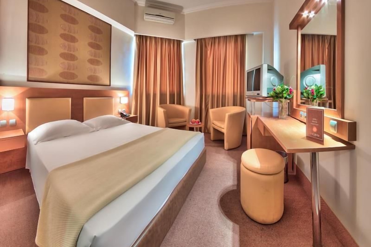 A hotel room with a bed, a desk, a chair, a TV, and a mirror.