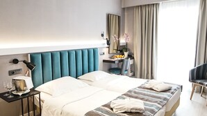 A hotel room with a large bed, a bedside table with a lamp, a small desk with a mirror, and a chair.