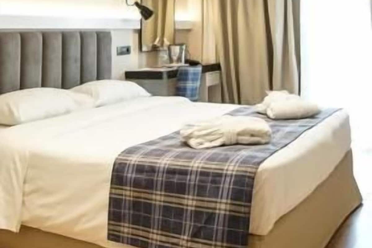 A modern hotel room with a large bed, a desk, and a window with curtains.