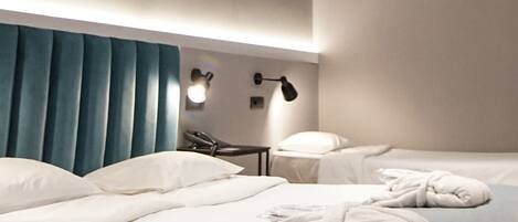 A modern hotel room with two beds, a blue headboard, bedside lamps, and a ceiling light fixture.
