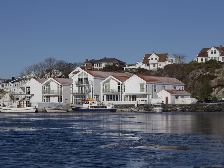 Een pand aan het water met meerdere huizen, een steiger met boten en een rotsachtige kustlijn.
