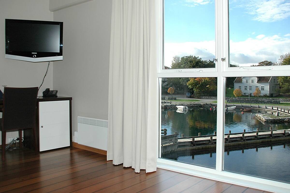 A room with a large window overlooking a marina, a flat-screen TV mounted on the wall, and a small desk with a telephone.