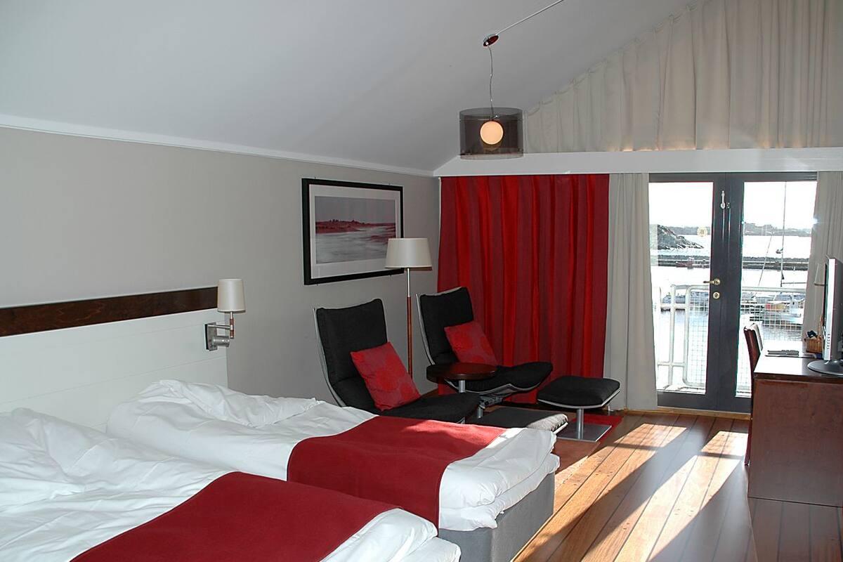 A hotel room with two beds, a desk, a chair, and a view of the sea.