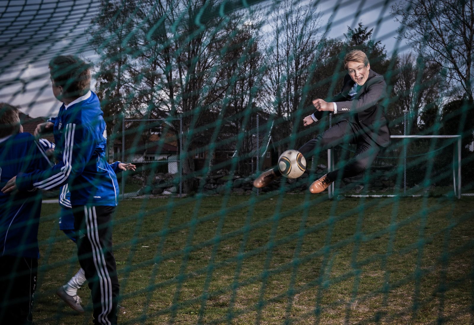 Un futbolista con traje negro pateando una pelota cerca de una red de portería.