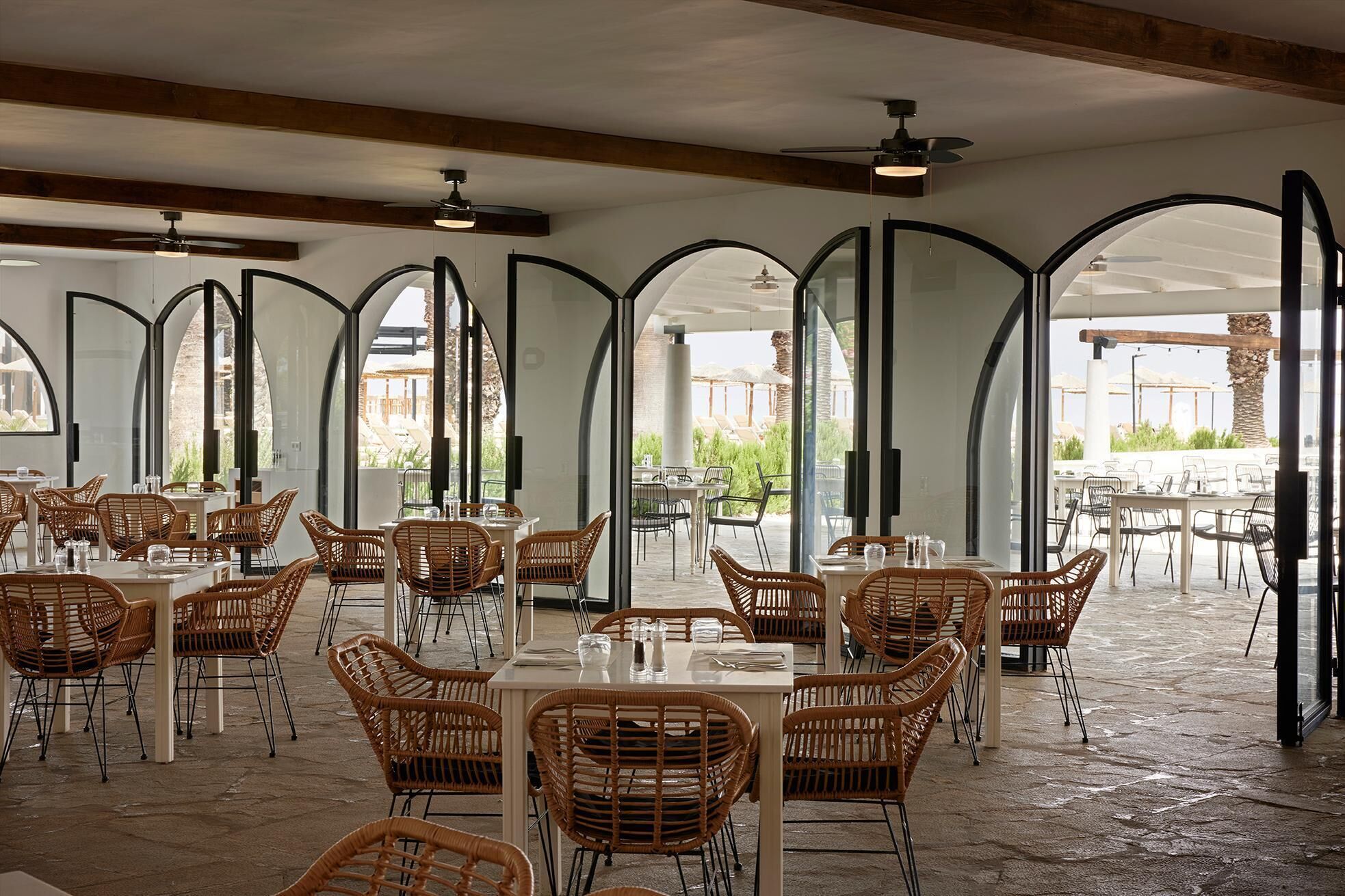 An indoor dining area with high arched ceilings, wicker chairs, and tables.