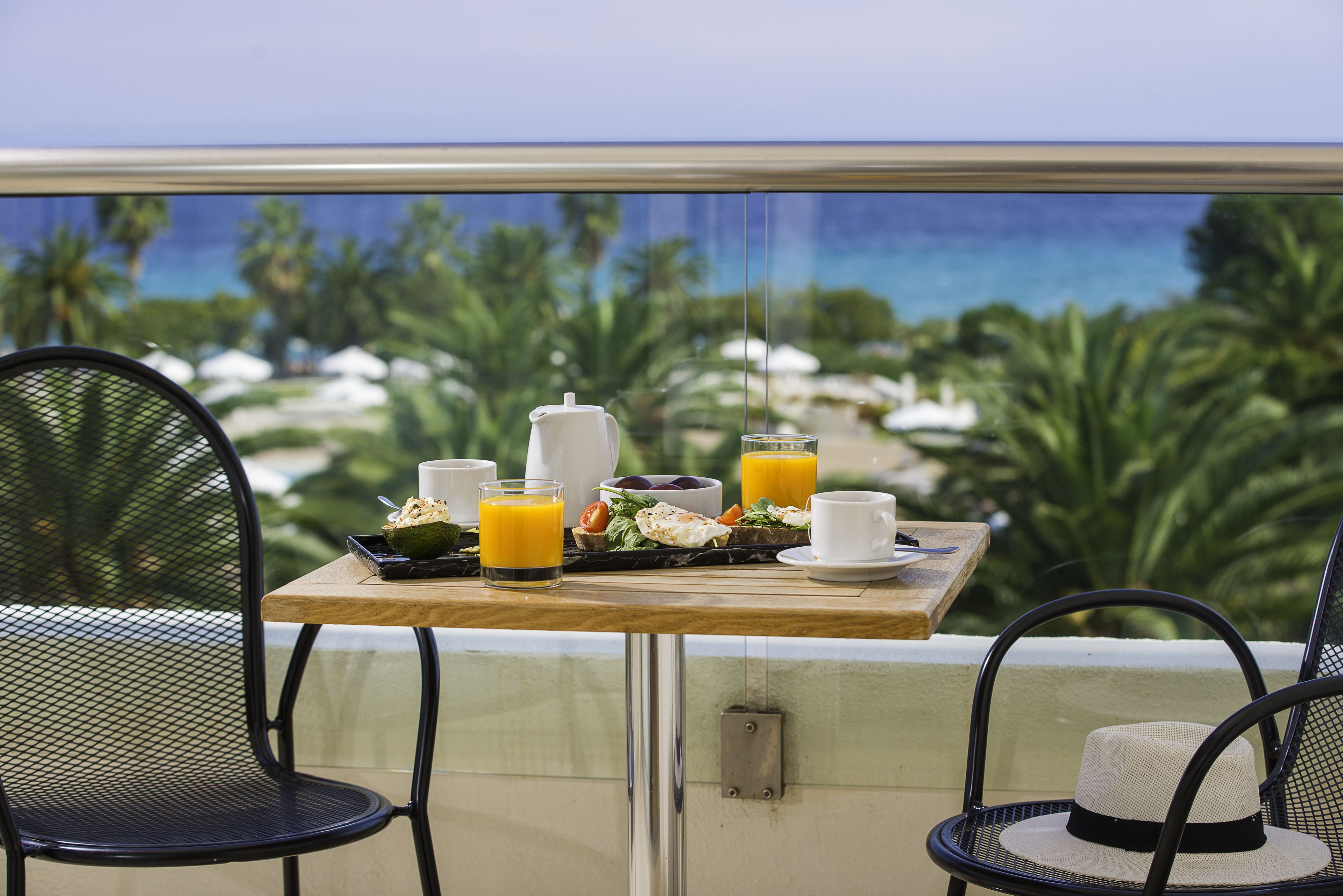 Ein Balkon mit einem Tisch, gedeckt für das Frühstück, einschließlich einer Tasse, einer Schüssel mit Müsli, einem Glas Orangensaft und einem Teller Essen.