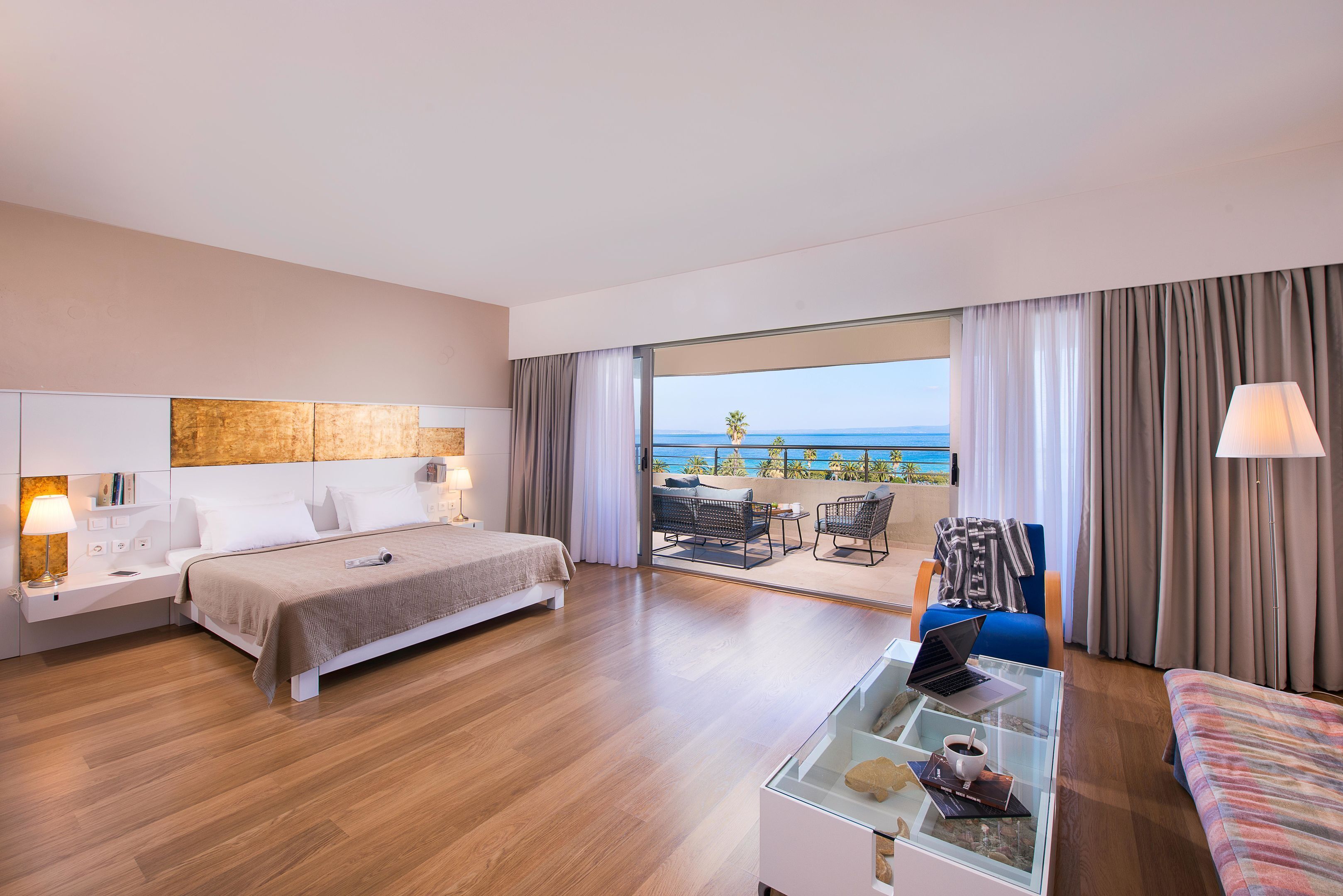 Habitación de hotel moderna con una cama grande, un escritorio con una computadora portátil, una mesa de centro de vidrio y vistas al mar.