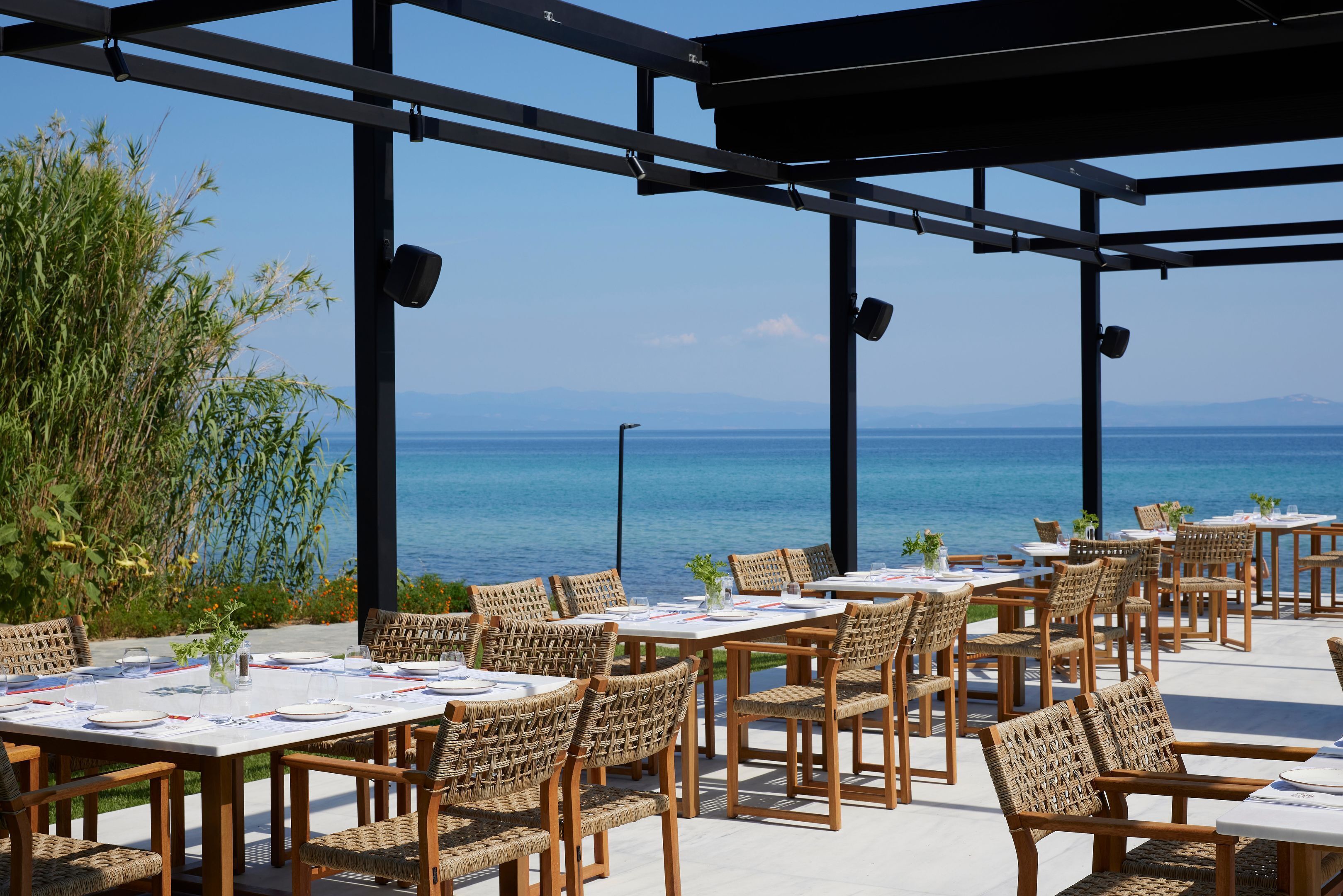 Zona pranzo all'aperto con sedie e tavoli in vimini, con vista su un lago e montagne.