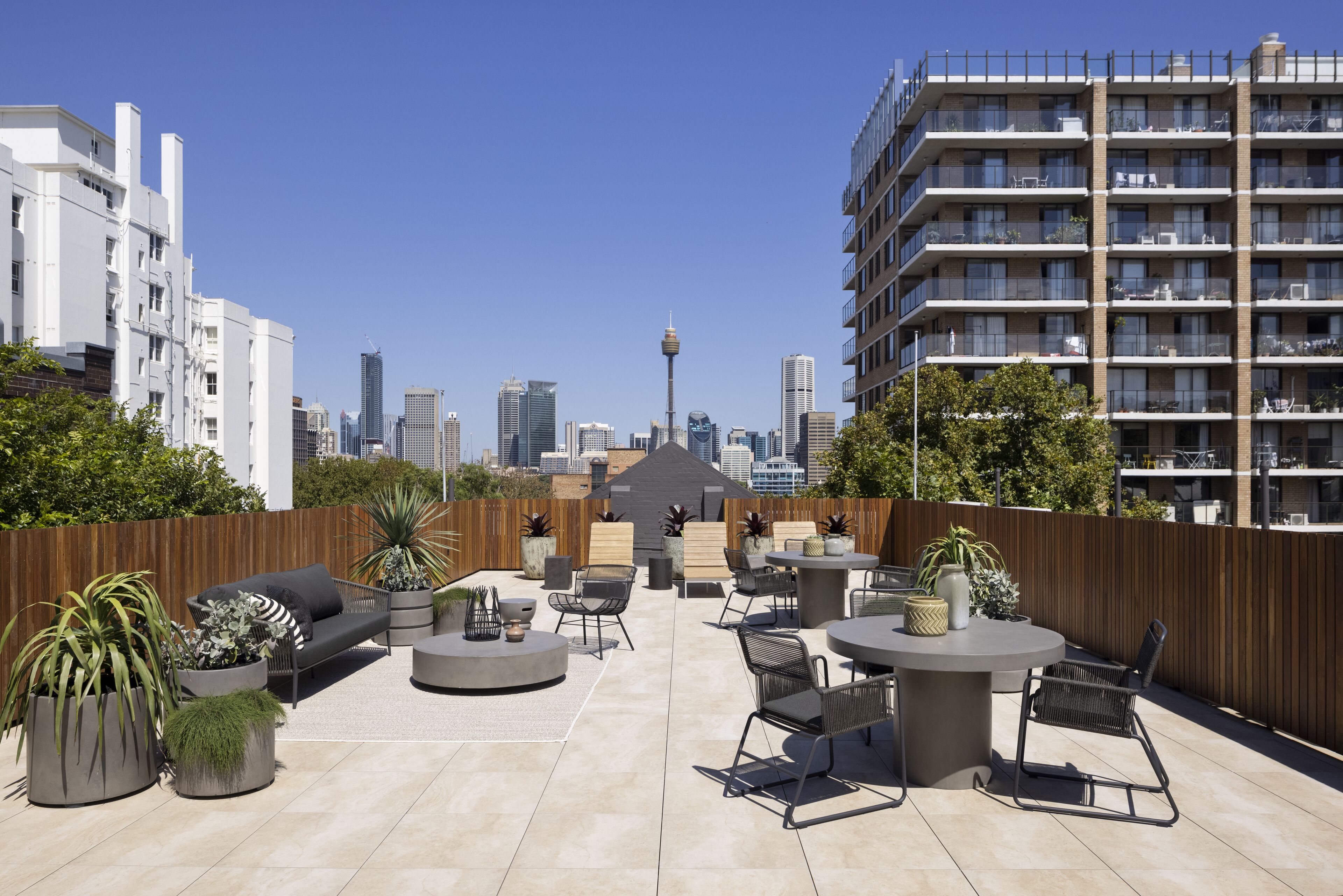 A rooftop patio with outdoor seating, potted plants, and a city skyline view.