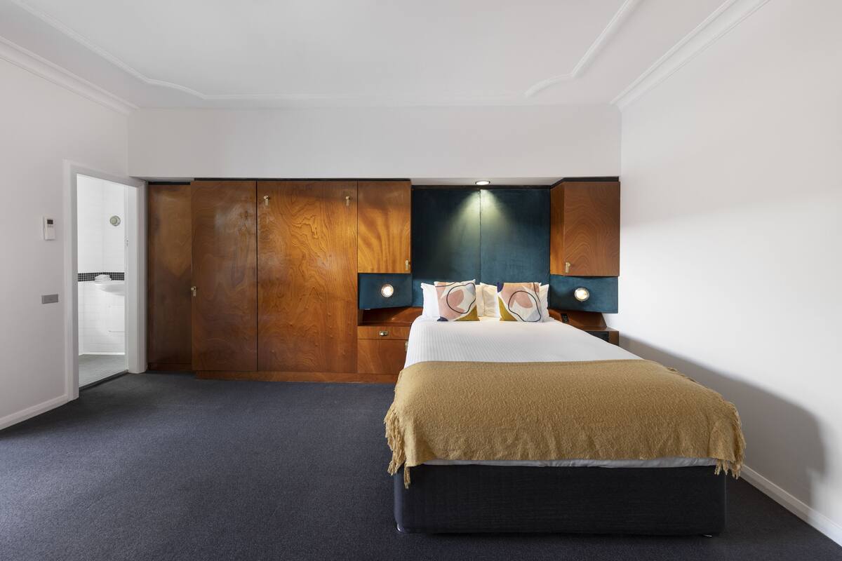 A hotel room with a large bed, wooden wardrobe, and a small bedside table.