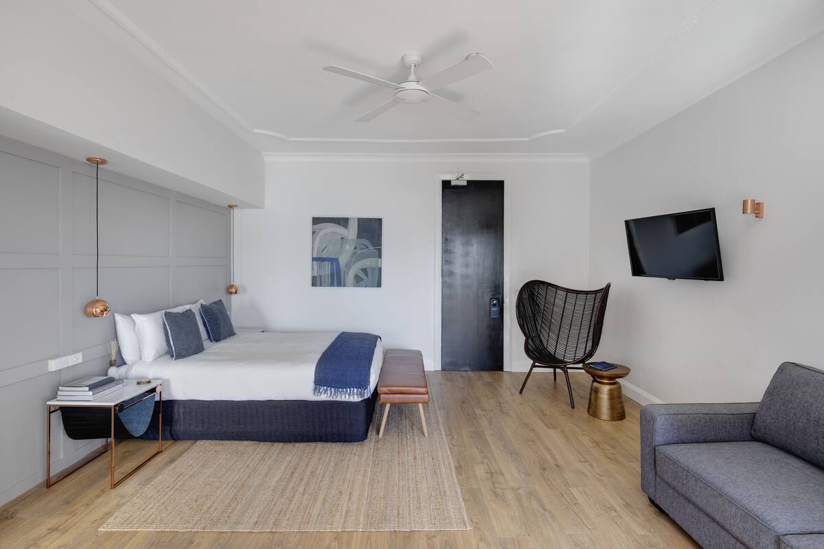 A modern bedroom with a bed, bedside table, chair, and a television on the wall.