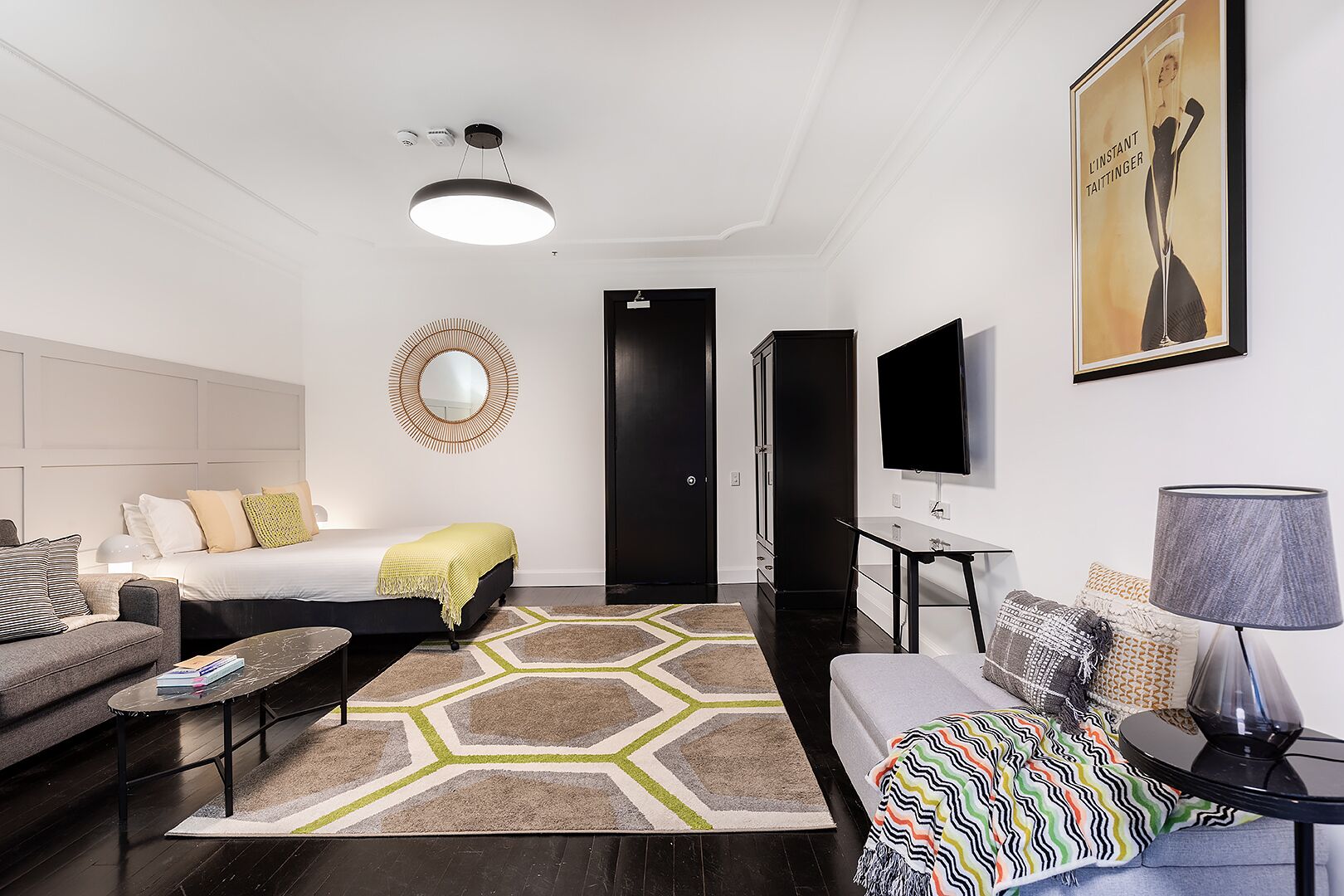A modern hotel room with a bed, sofa, TV, and a desk.