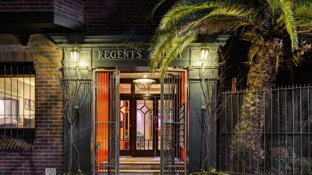 Entrada de un edificio con el nombre "REGENTS" sobre la puerta, un acceso con portones y dos macetas grandes a cada lado.