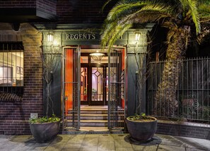 A building entrance with the name "REGENTS" above the door, a gated entrance, and two large planters on either side.