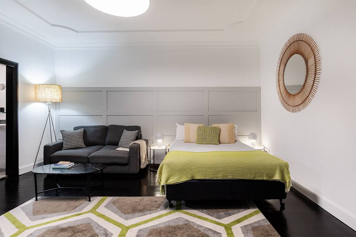 A modern bedroom with a sofa, a bed, a bedside table, a lamp, and a decorative mirror.