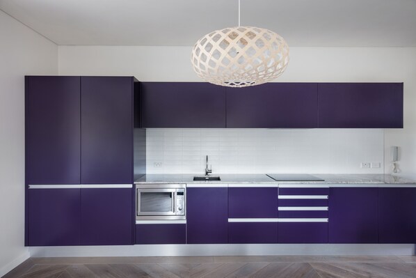 A modern kitchen with purple cabinets, a stainless steel microwave, and a white tiled backsplash.