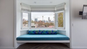 Un ventanal con un banco azul acolchado, vistas a la ciudad y un televisor montado.