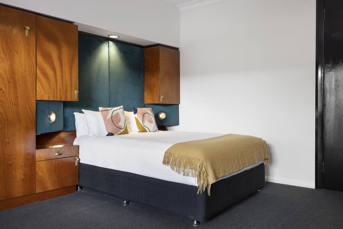 A bedroom with a bed, wooden wardrobe, and a dark-colored headboard.