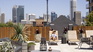 Un área de estar al aire libre con sillones reclinables y macetas, una valla de madera y un horizonte urbano de fondo.