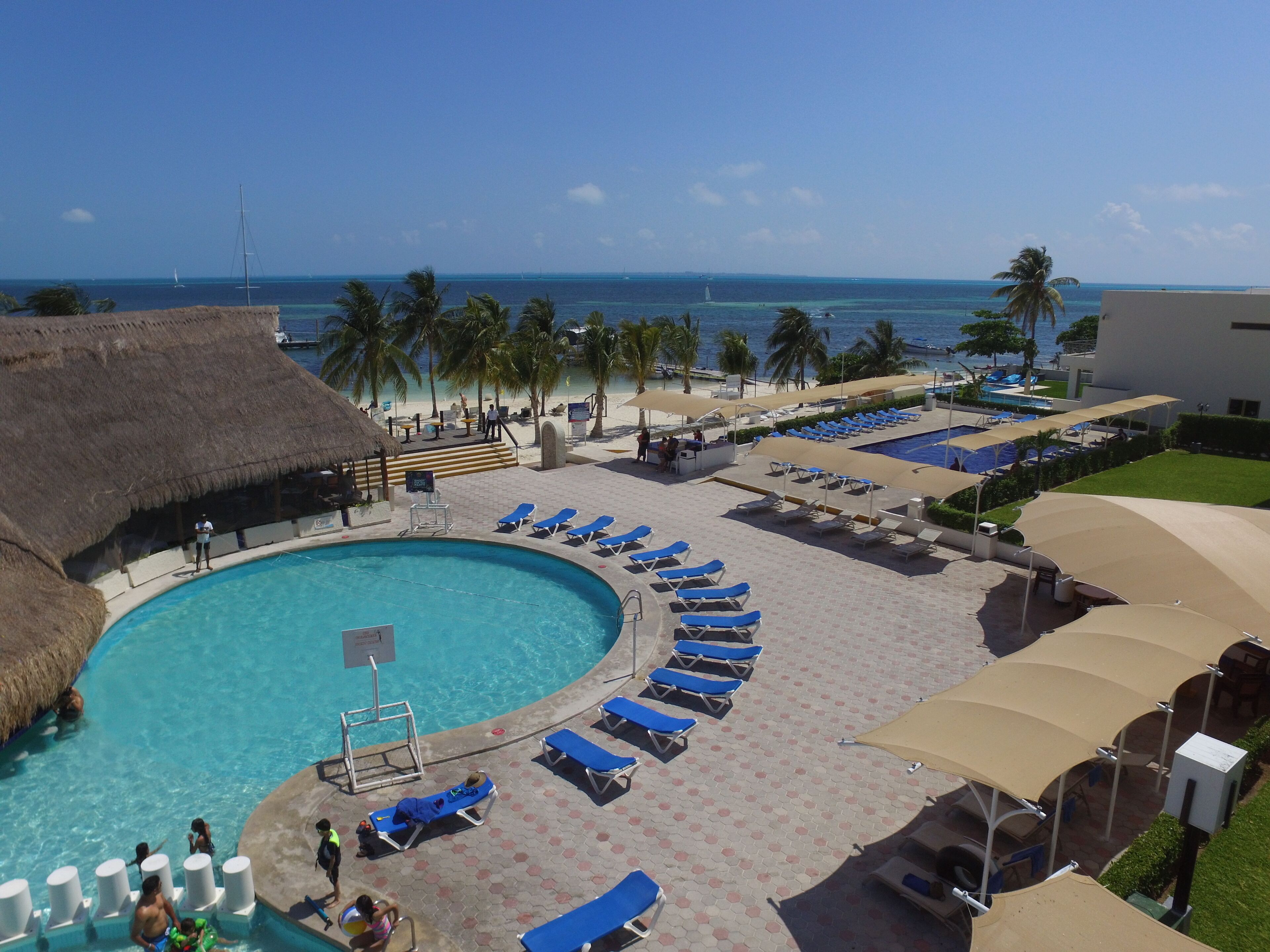 Zwembadgedeelte van een resort met een rond zwembad, ligbedden, palmbomen en uitzicht op de oceaan.