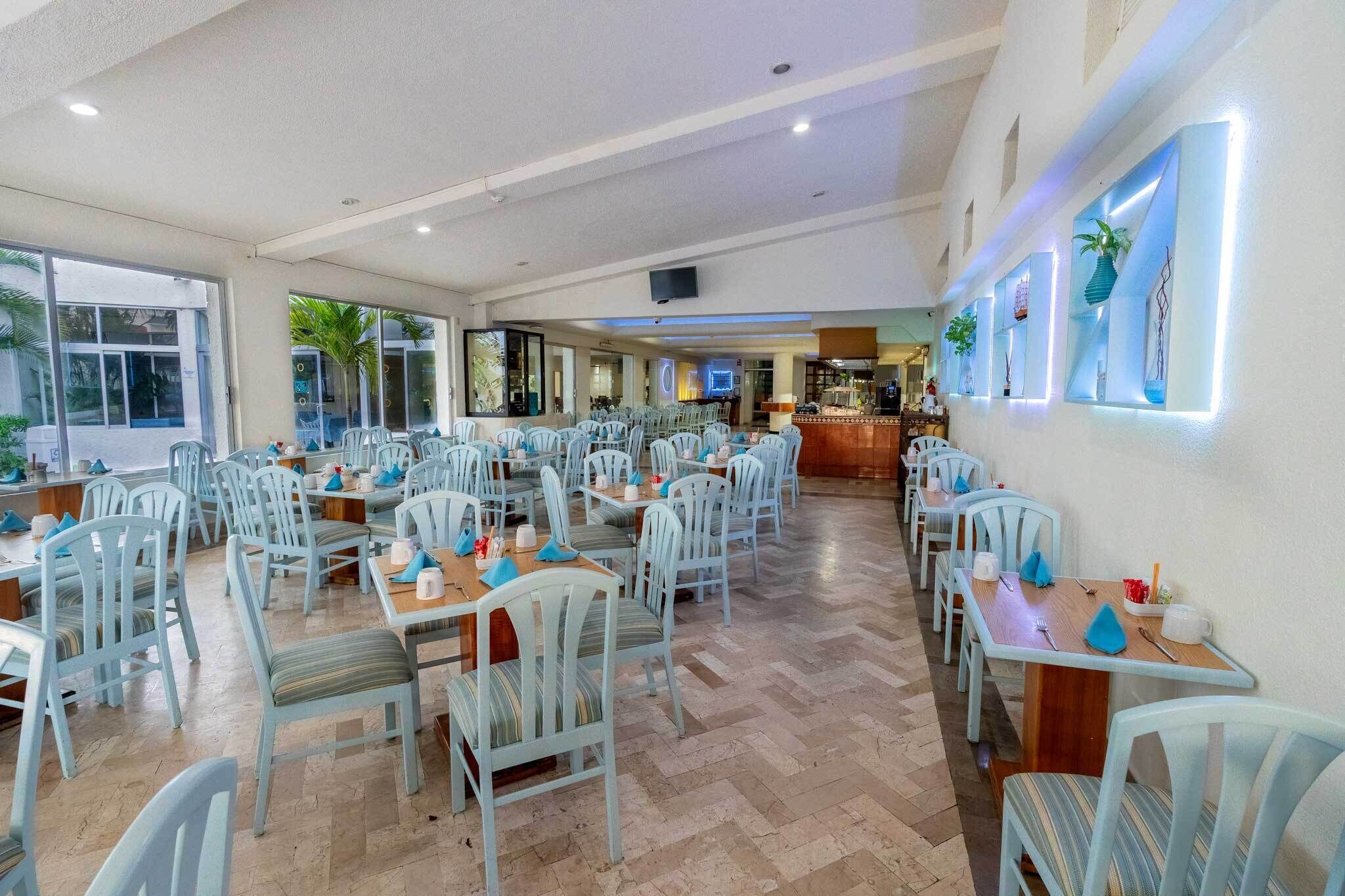 A spacious dining area with multiple tables and chairs, a bar area, and large windows providing natural light.