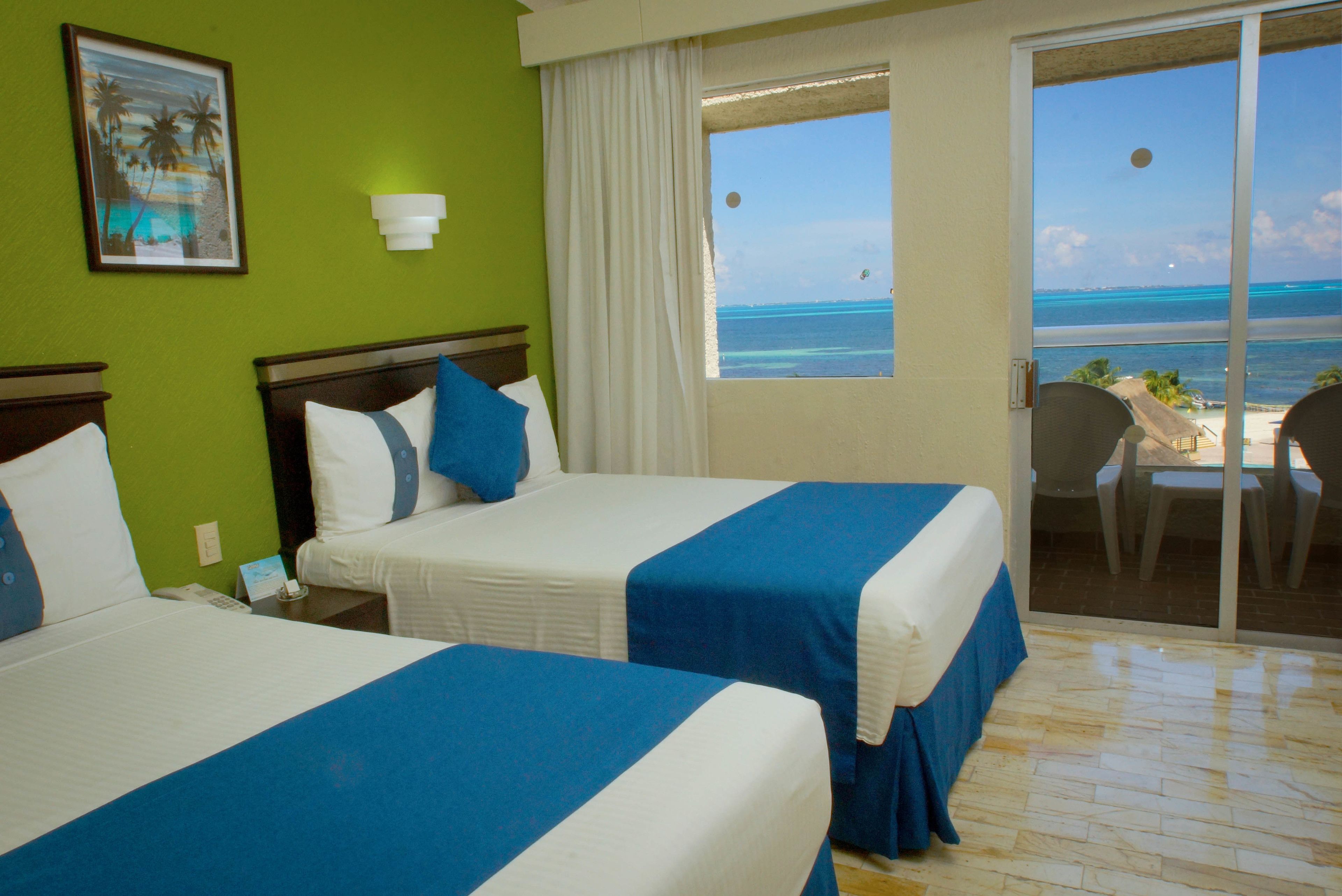 Une chambre d’hôtel avec deux lits, une vue sur l’océan et un balcon équipé de chaises.