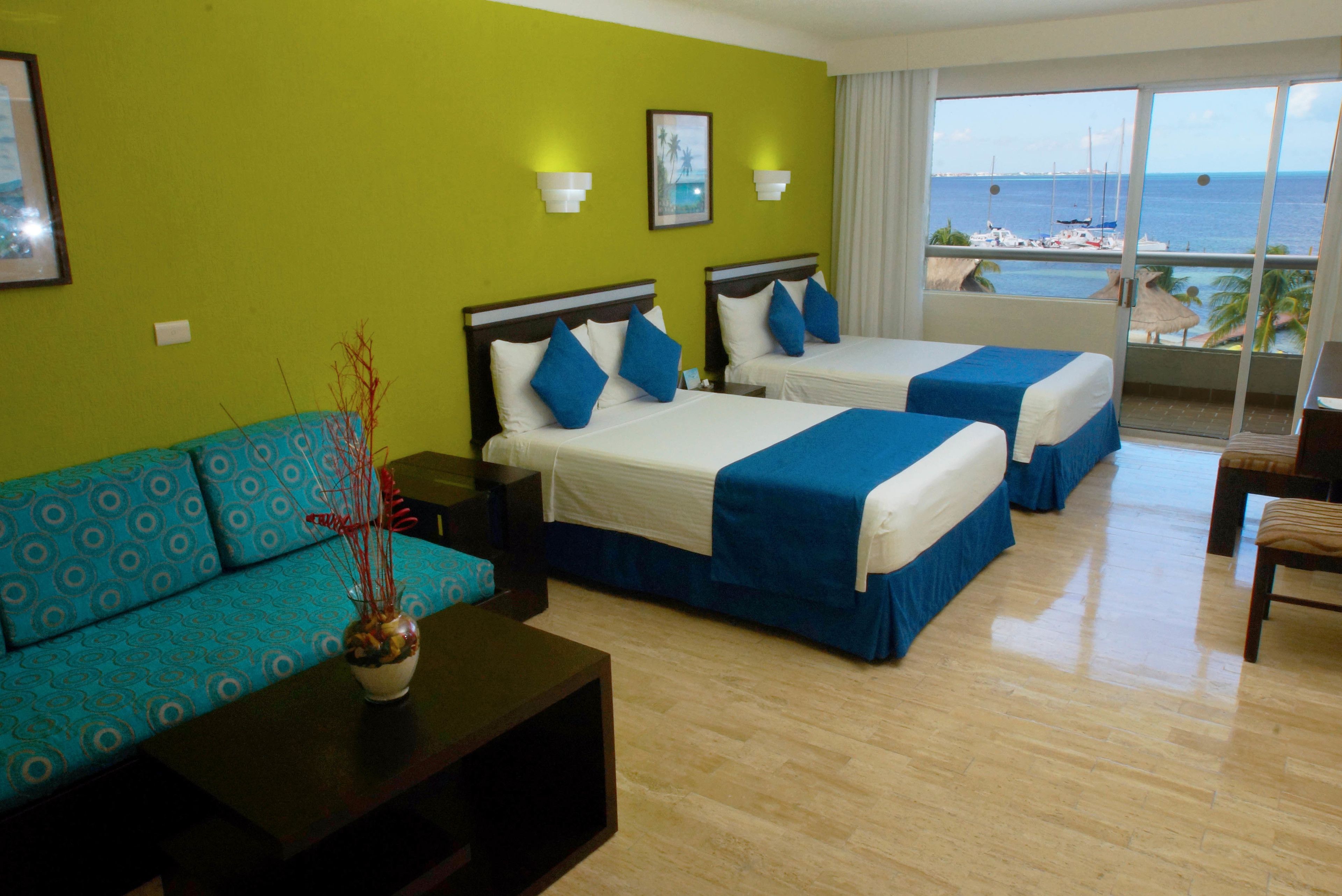 A hotel room with two beds, a sofa, a coffee table, and a view of the sea.