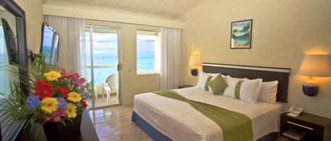 A hotel room with a bed, a desk with a lamp, a phone, and a view of the ocean.