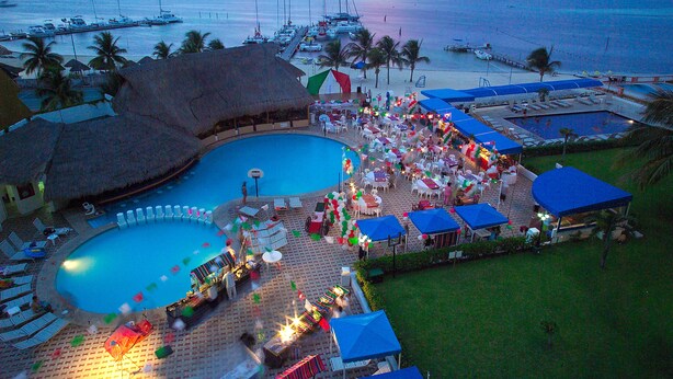 Un resort con una grande piscina, lettini e una spiaggia attrezzata con barche.
