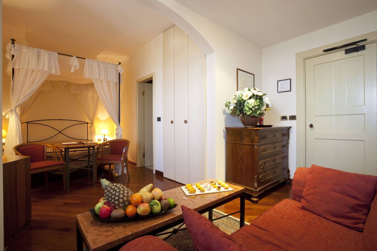 Ein gemütliches Wohnzimmer mit Essbereich, einer Holzkommode und einem Bett mit weißen Vorhängen.