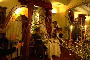 A dining area with a harp, a table set for four, and a waiter attending to guests.