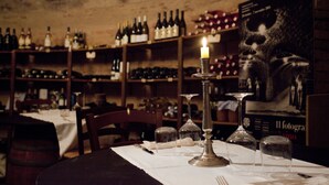 A dimly lit room with a table set for dining, surrounded by shelves of wine bottles. - Hotel Monte del Re (Dozza)
