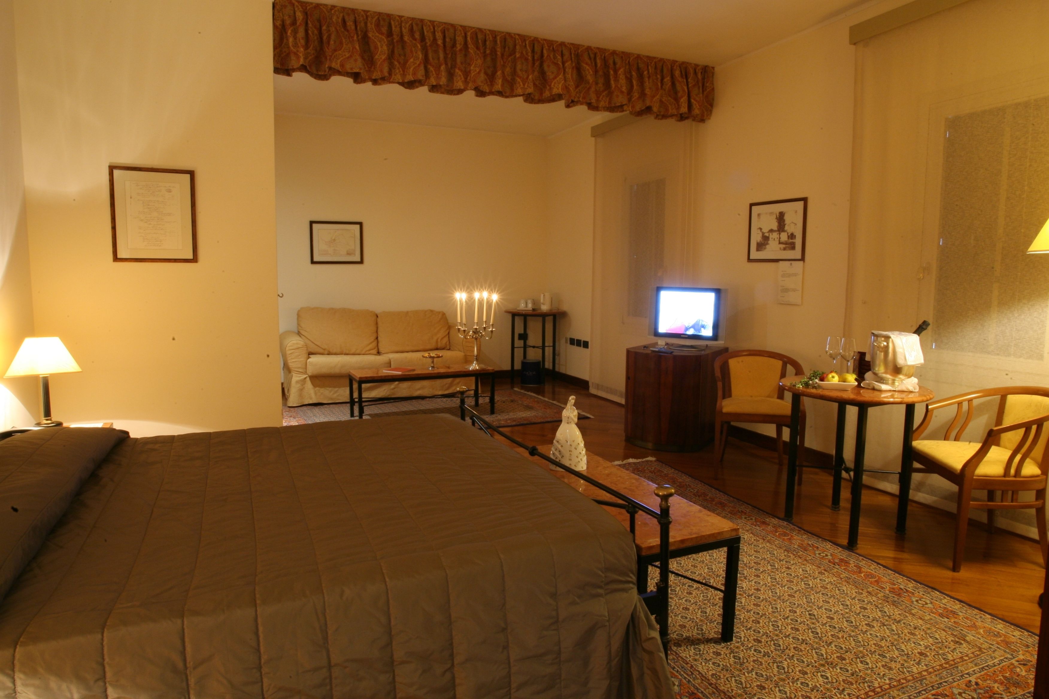A hotel room with a large bed, a sofa, a small table with a lamp, a television, and a chair.