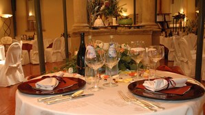 A formal dining table set with wine glasses, plates, and cutlery, surrounded by chairs with white covers. - Hotel Monte del Re (Dozza)