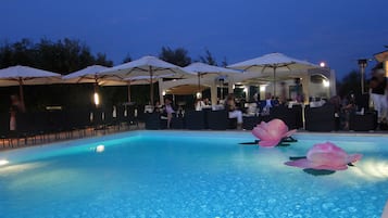 A pool area with lounge chairs and umbrellas, surrounded by a covered seating area with tables and chairs.