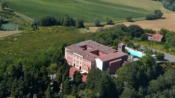 An aerial view of a large building with a red roof, surrounded by lush greenery and fields.