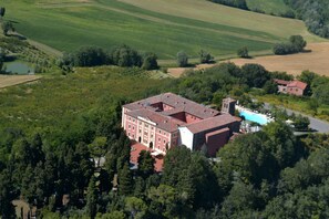 An aerial view of a large building with a red roof, surrounded by lush greenery and fields.