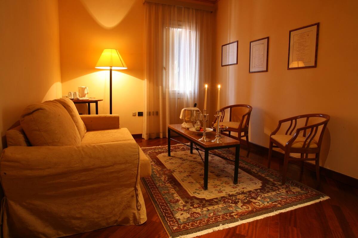 Ein gemütliches Hotelzimmer mit einer Couch, einem kleinen Tisch mit Kerzen, einer Lampe und einem Sessel.