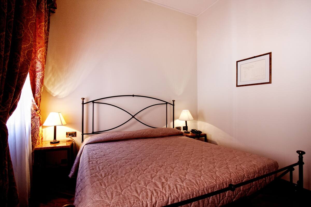 Ein ordentlich bezogenes Bett mit Kopfteil, zwei Nachttischlampen und einem gerahmten Zertifikat an der Wand.