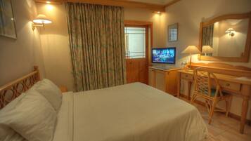 Una habitación de hotel con una cama, un escritorio con computadora, una silla y una ventana con cortinas.