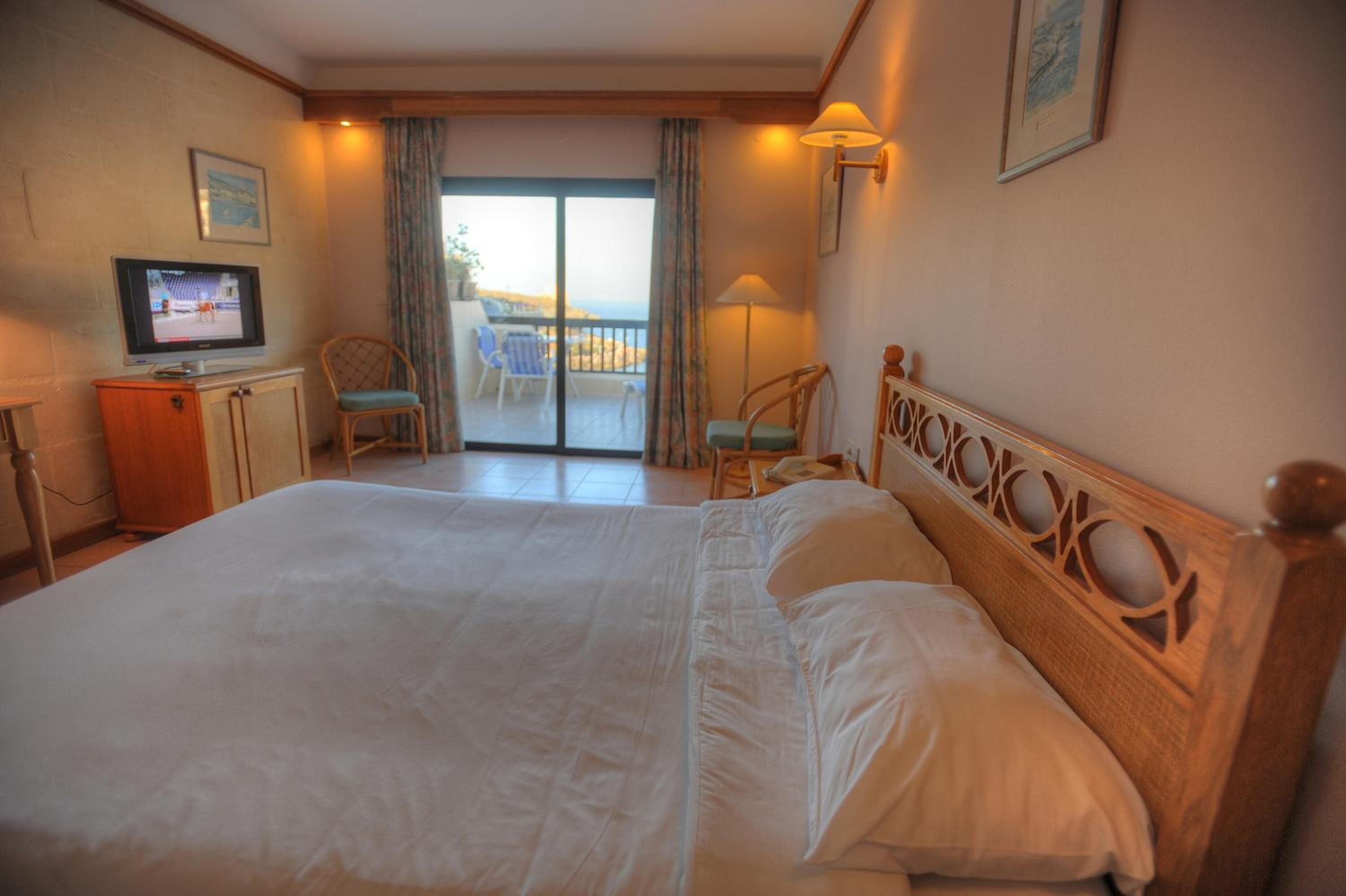Habitación de hotel con una cama grande, televisión, escritorio y balcón con vistas.